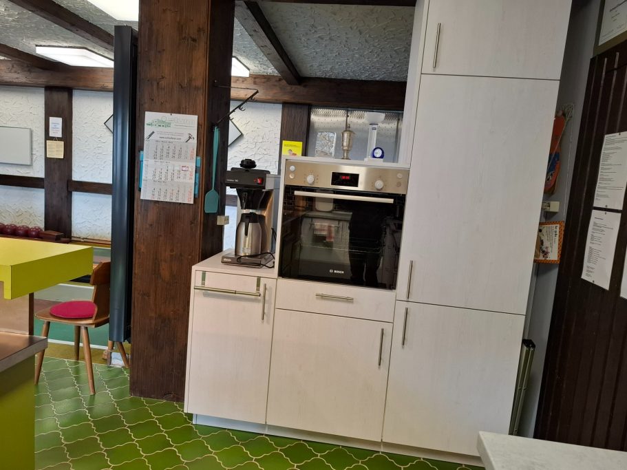 Küchenzeile Moderne Küche mit Backofen, Kaffeemaschine und weißen Schränken. Grüner Boden.